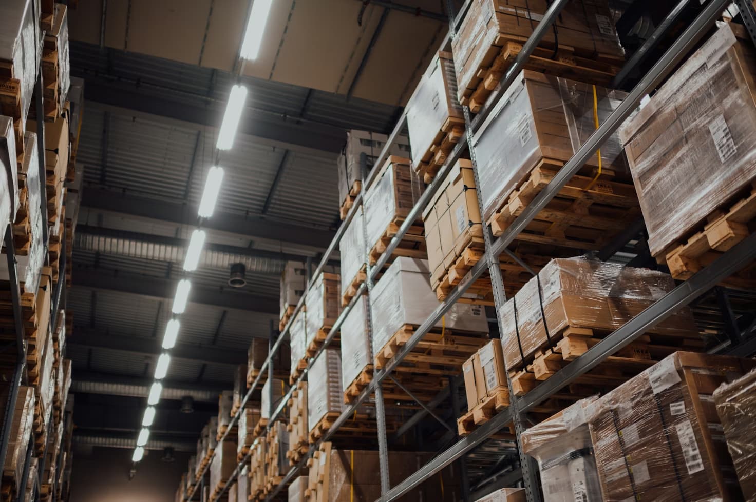 Pasillo de racks de almacén industrial con tarimas estibadas a varios niveles